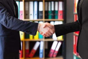 a HR consulting firm employee and an executive of a prospective client shake hands